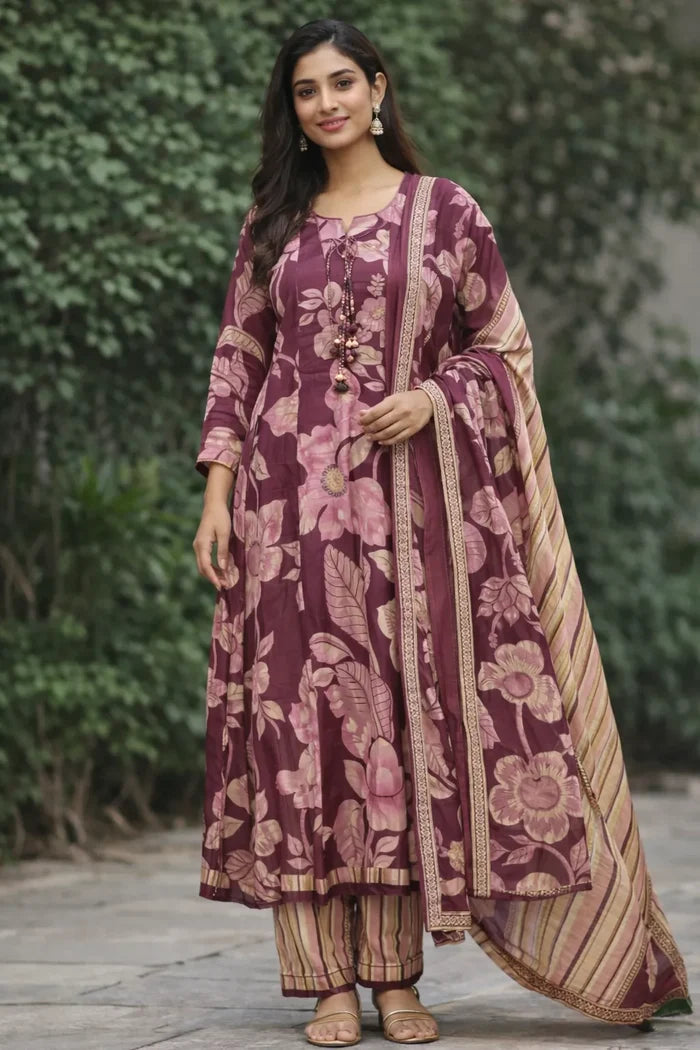 Woman wearing a traditional maroon and gold outfit with floral patterns against a green foliage background.