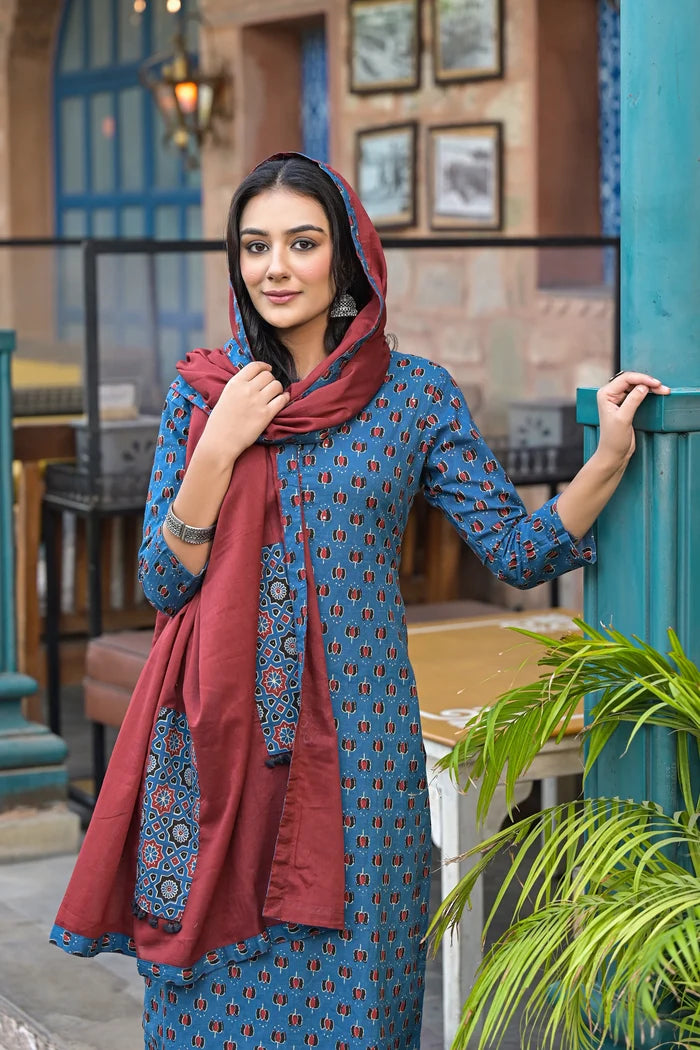 Woman in a blue patterned outfit with a red scarf standing outdoors.