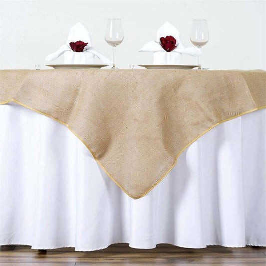 Burlap table runner with gold trim on a white tablecloth, set for dinner.