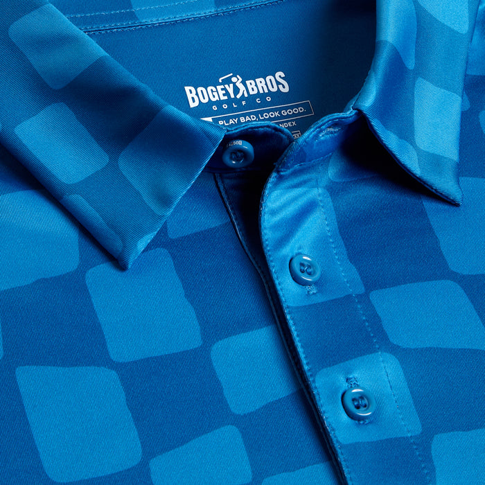 Close-up of the Checked Out - Polo, a blue collared shirt featuring a geometric pattern of lighter blue squares, three matching buttons, BOGEY BROS CLASSIC label, and moisture-wicking fabric with a smooth, slightly shiny finish.