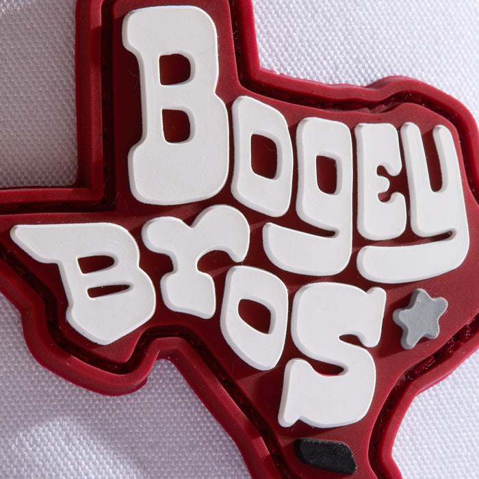 A red patch shaped like Texas features bold, white, bubble-style text reading “Bogey Bros.” on a textured white background. A small gray star and black shape appear near the bottom right of the patch.