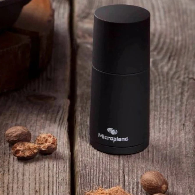 Black microplane grater on a wooden surface with nuts and nutmeg