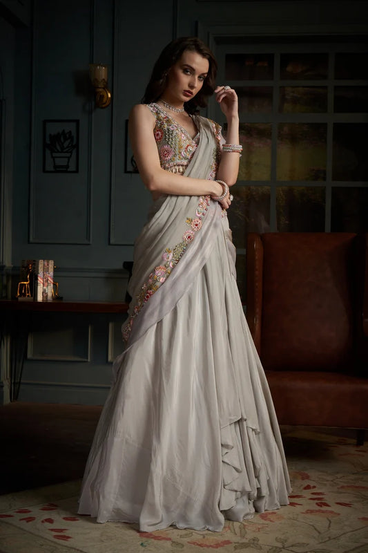 Woman in a floral saree standing in a room with a couch and decorative items.