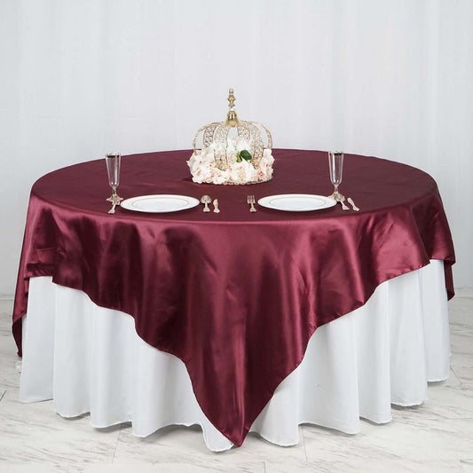 Round burgundy tablecloth on a dining table set with plates and a decorative crown.