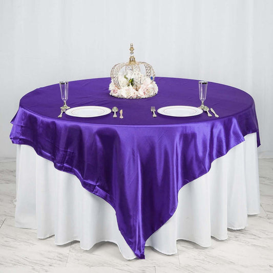 Purple satin tablecloth draped over a round table with elegant tableware.