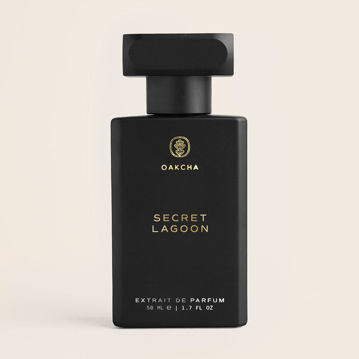 Front view of Secret Lagoon perfume showing matte black rectangular bottle with gold logo and black cap on beige background
