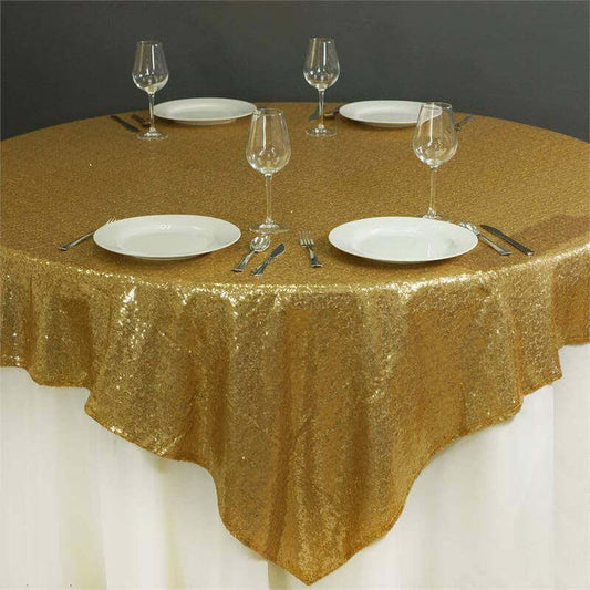 Gold sequin tablecloth on a round table set for dining with plates and glasses.