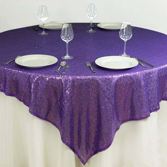 Purple sequin tablecloth on a round table set with plates and glasses.