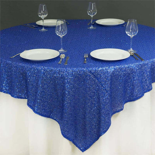 Round blue sequin tablecloth on a dining table with plates and glasses.