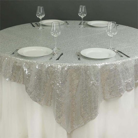 Silver sequined tablecloth on a round table set with plates and glasses.