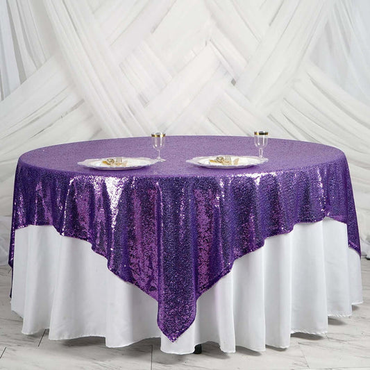 Purple sequin tablecloth draped over a round table with plates and glasses.