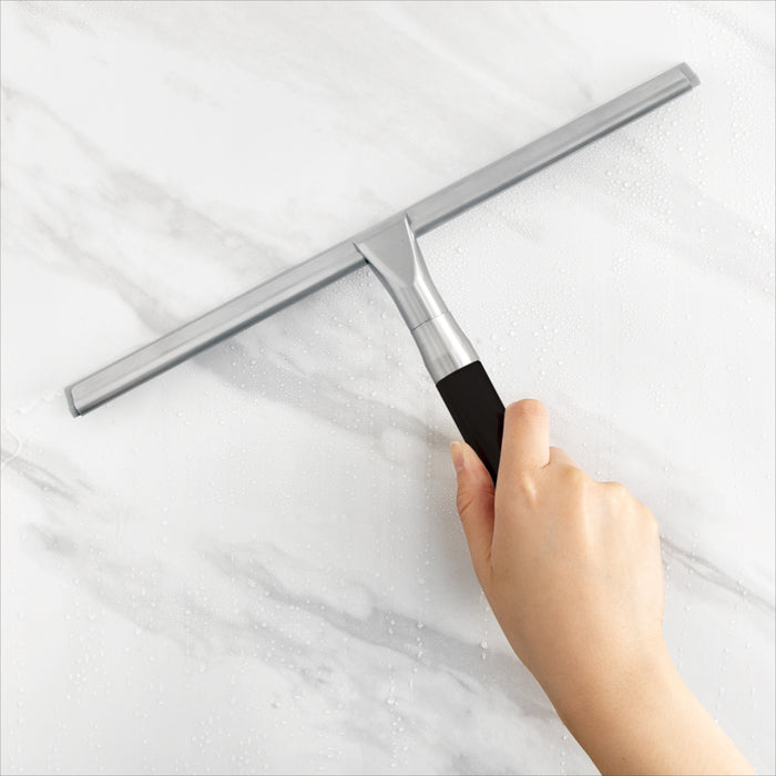 Zadro ZSQ912 705004423403 environment photo front view on marble wall user holding handle, shower squeegee with silicone blade & wall mounting bracket in front of a real life setting