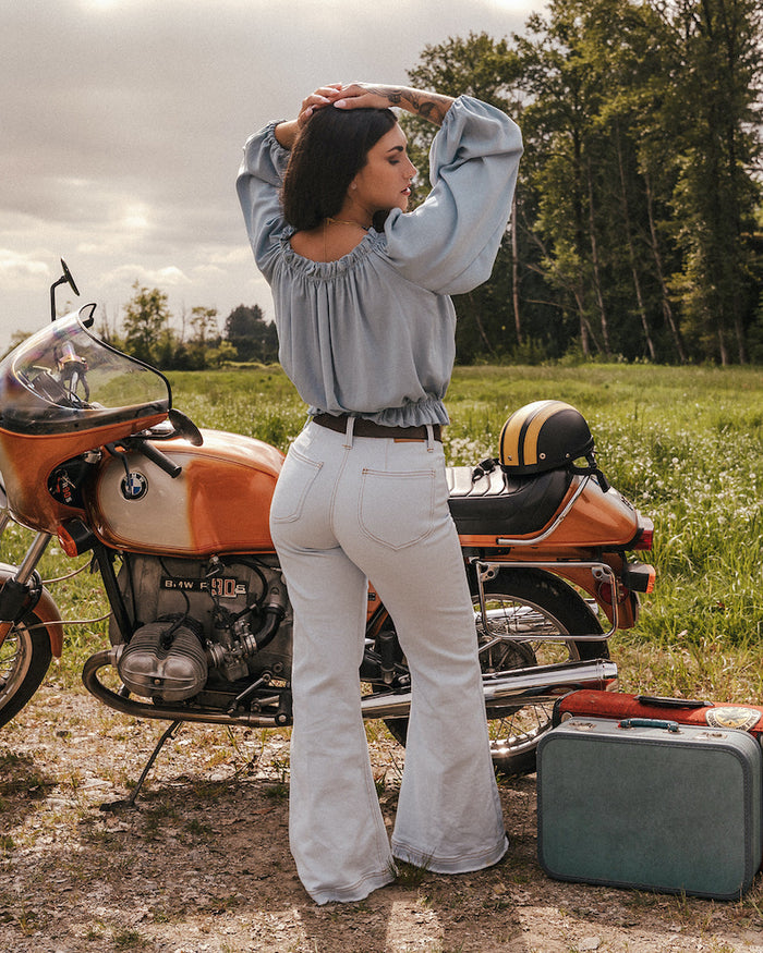 Woman standing next to a motorcycle in a field with a suitcase nearby wearing a sweet Jane peasant blouse by Soul Sister since 1969