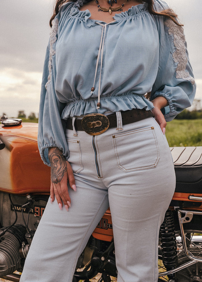 Person wearing a light blue top and sun faded denim bell bottom jeans designed by Soul Sister since 1969 standing next to a vintage motorcycle.