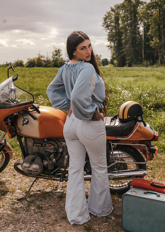 Woman standing next to a vintage motorcycle in a field wearing Soul Sister since 1969