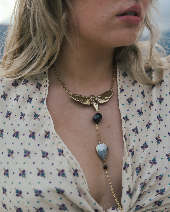 Close-up of a woman wearing a gold necklace with a butterfly pendant and black beads wearing Soul Sister since 1969..