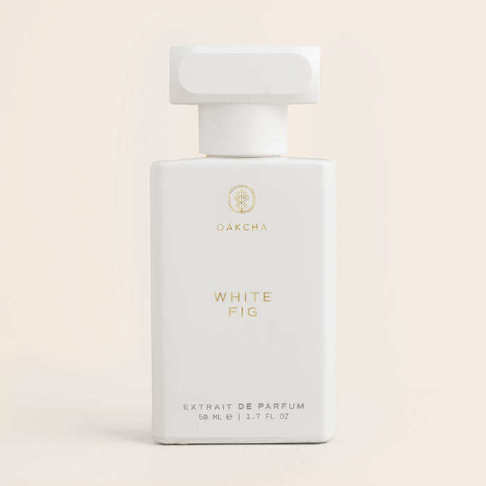 Front view of White Fig perfume bottle showing matte-white bottle with gold logo labeled WHITE FIG on pale beige background