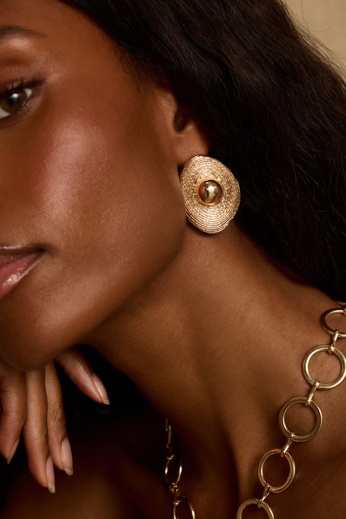 Close-up of textured gold statement stud earring worn with a gold circle-link necklace.